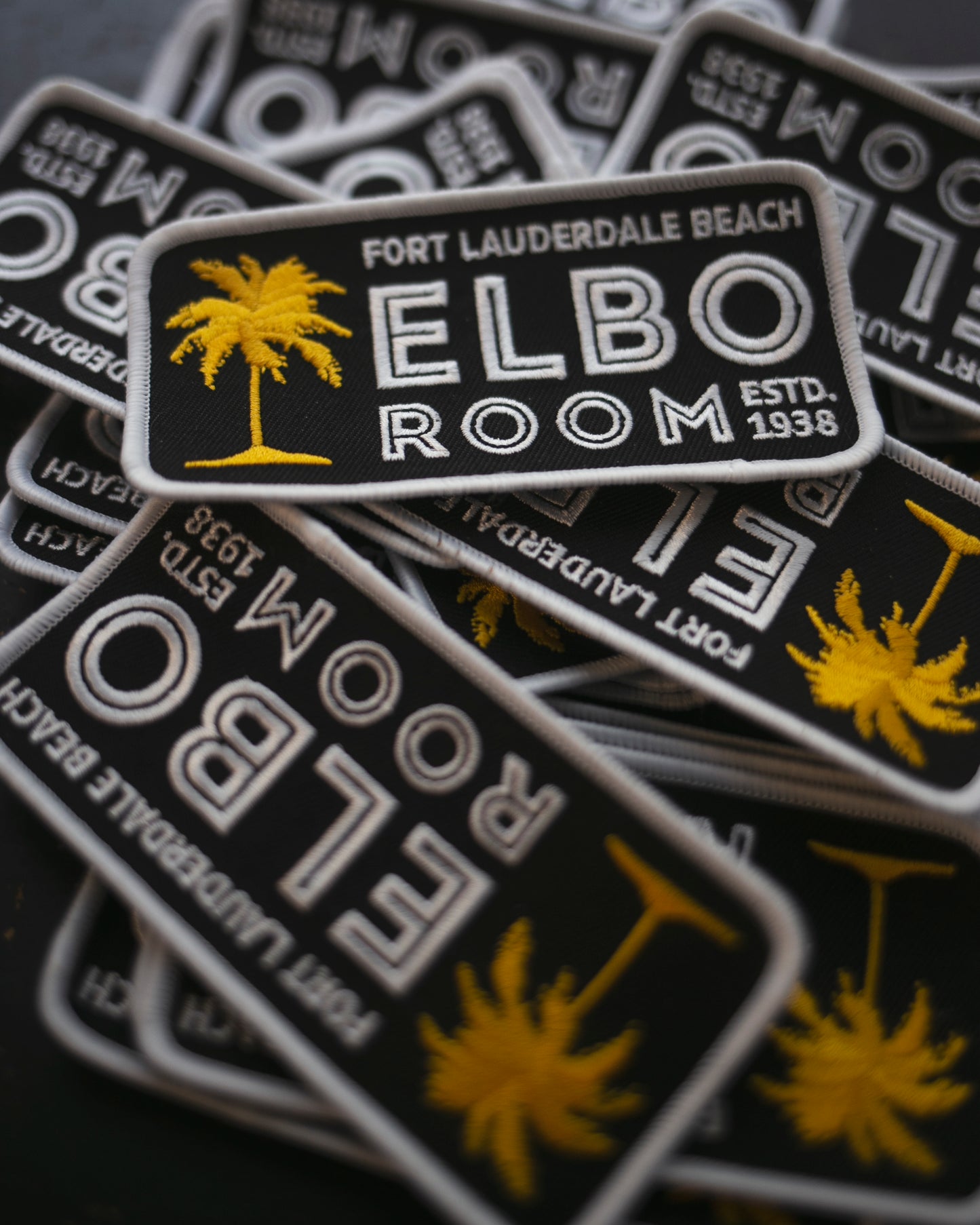 Stack of 'Fort Lauderdale Beach ELBO Room' patches with palm tree design on a dark background