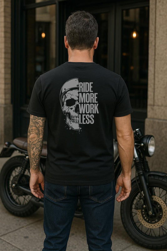 "Man wearing black t-shirt with skull helmet graphic and 'Ride More Work Less' text, standing in front of a cafe racer motorcycle in an urban setting"