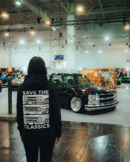 Person wearing a hoodie with 'Save the Classics' text in a car showroom featuring classic chevy trucks